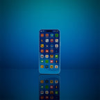 Blue plastic toy phone with a printed grid of colorful app icons on its screen, standing upright on a glossy blue reflective surface