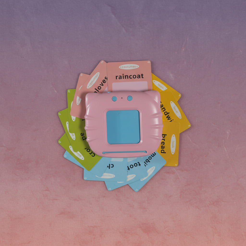 Overhead view of the pink learning machine surrounded by a fan of colorful flashcards printed with words like raincoat, gloves and bread